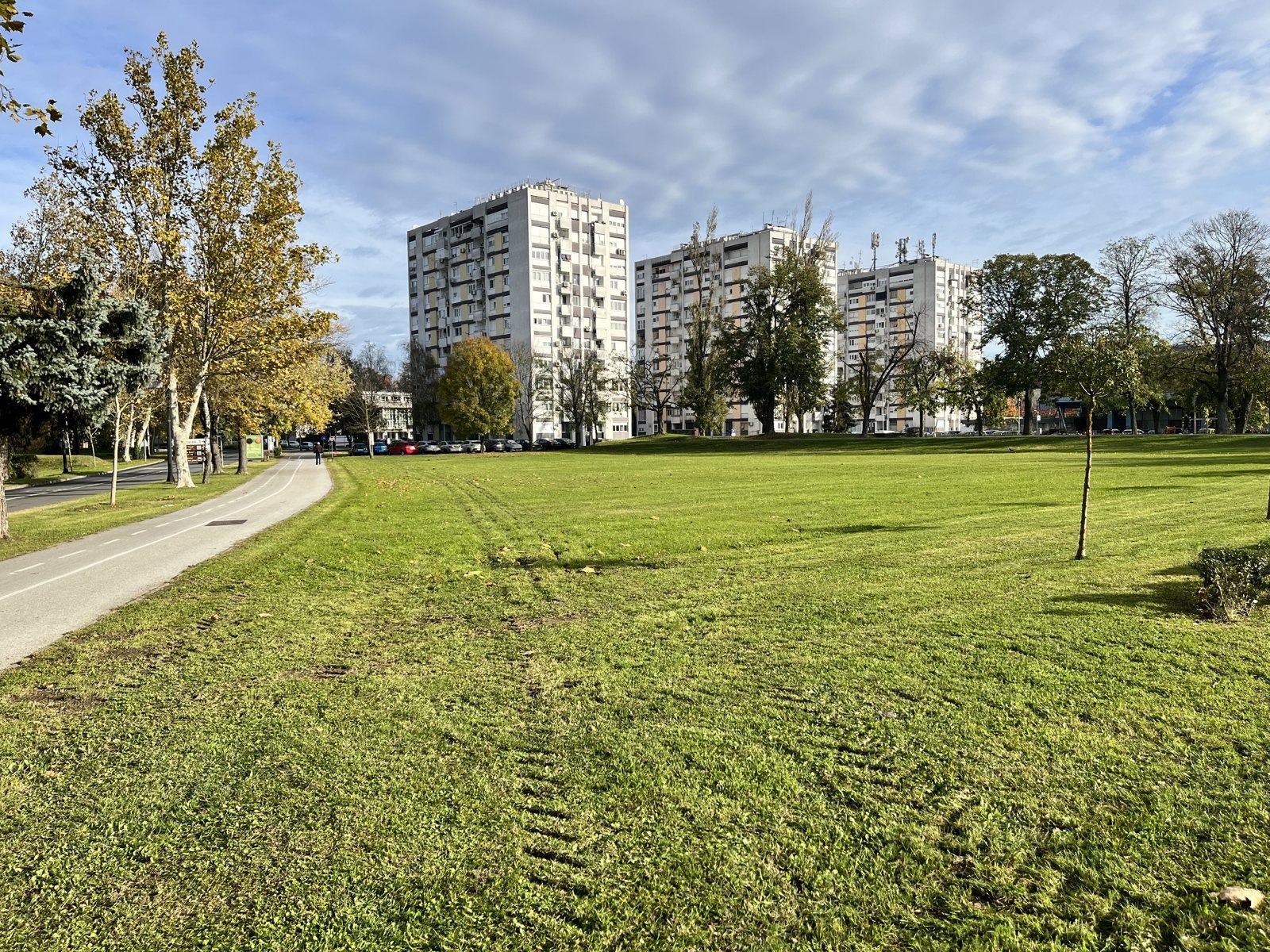 Park ob stanovanjskih blokih v Hrvaški s pasovi v travi po strojnem sajenju